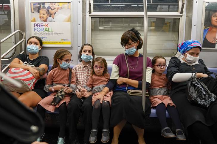 Family, some wearing face masks and some not, ride the subway, in the Brooklyn borough of New York.